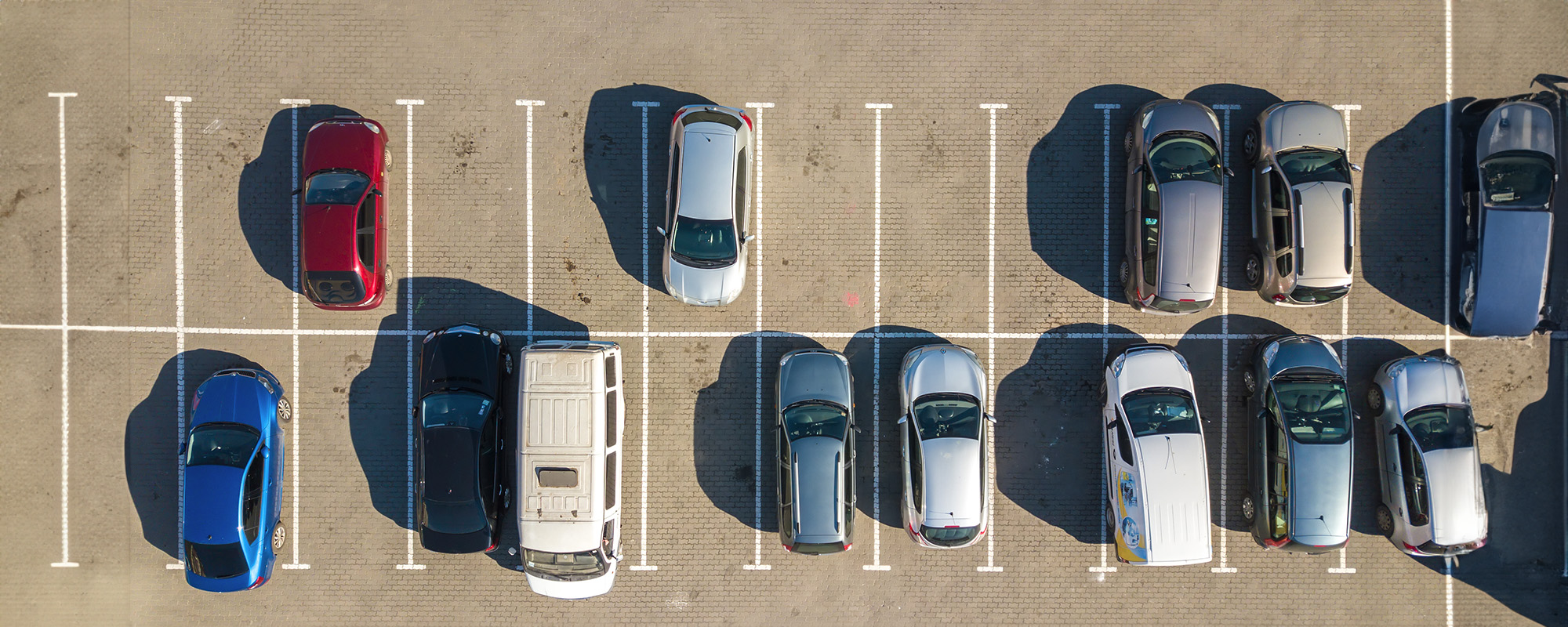 aerial view of many colorful cars parked on parking lot with lines and markings for parking places and directions
