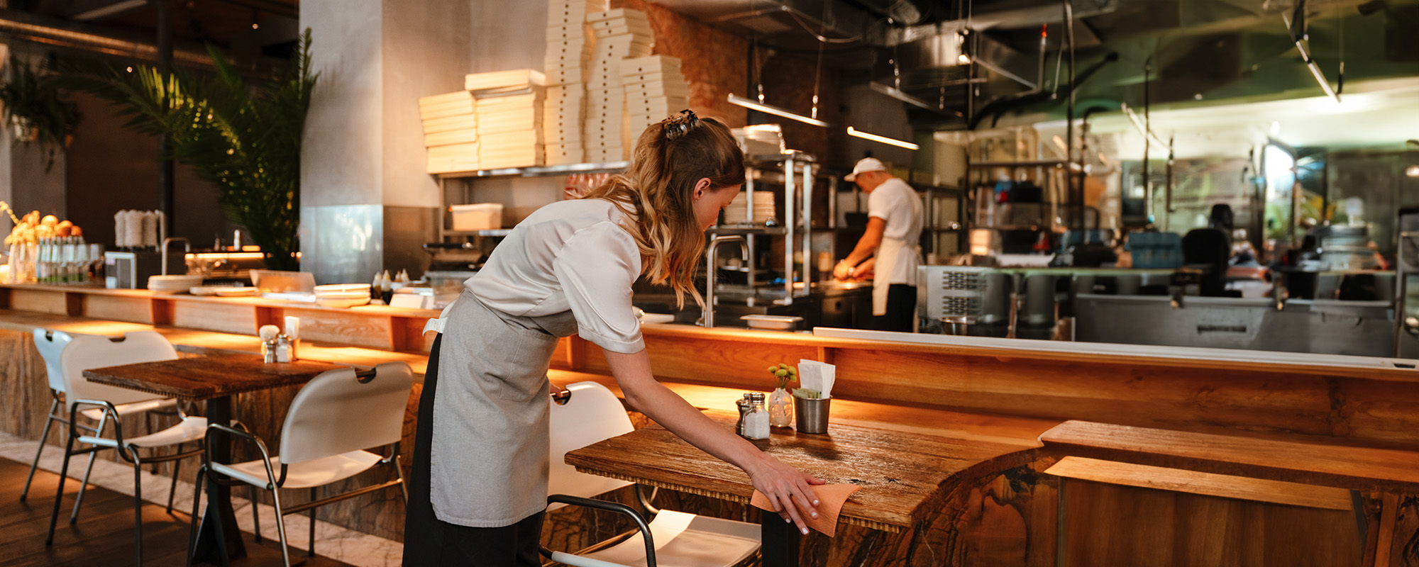 young woman waitress disinfecting table in restaurant