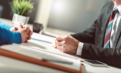 two people with hands folded at desk in negotiation