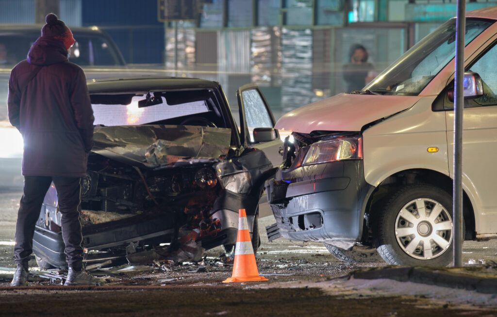 Cars crashed heavily in road accident after collision and silhouette of people on city street at night. Road safety and insurance concept.
